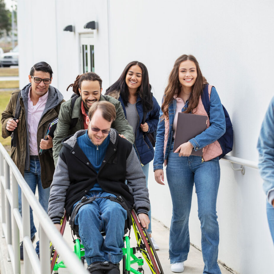 Group of six young people including a man in a wheelchair accessing a building via a ramp