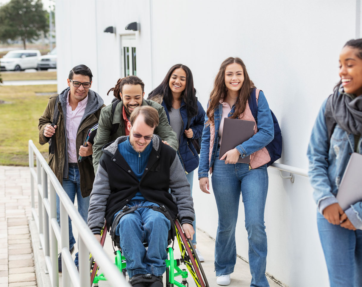Group of six young people including a man in a wheelchair accessing a building via a ramp